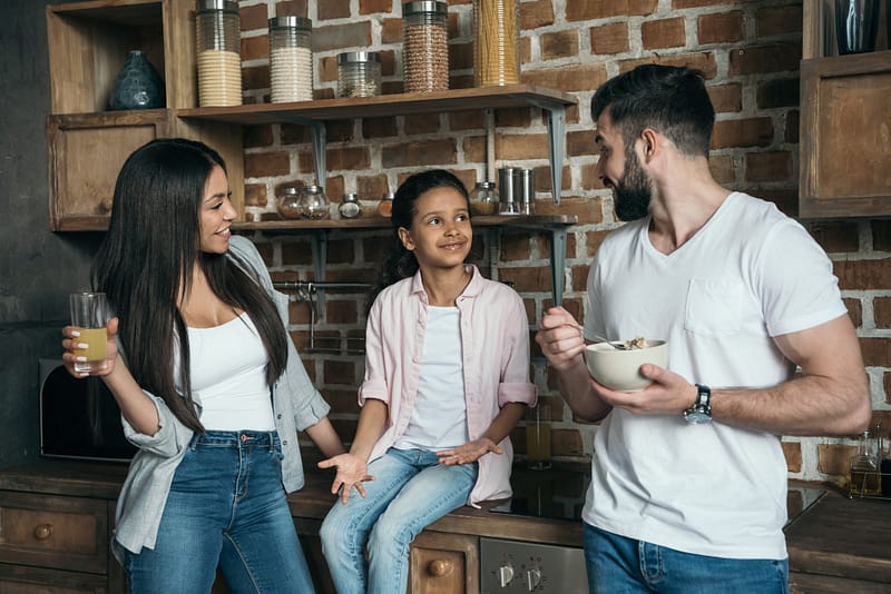 happy multiethnic family talking while having breakfast at kitchen