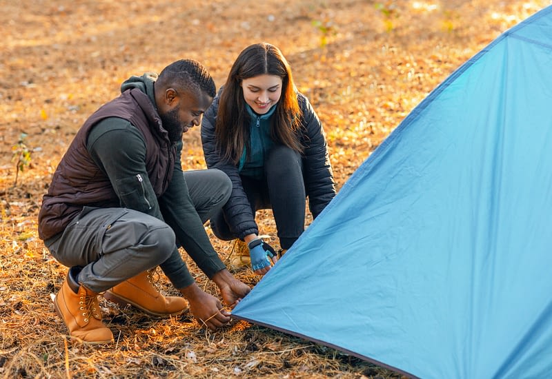 Multiracial young couple setting tent, camping together