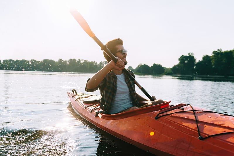 Man kayaking. Handsome young man kayaking on lake and smiling