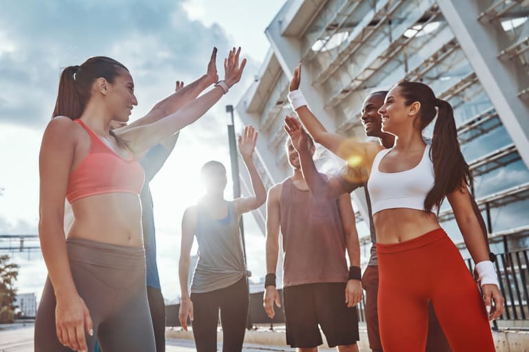 Group of young people in sports clothing encouraging each other while exercising outdoors