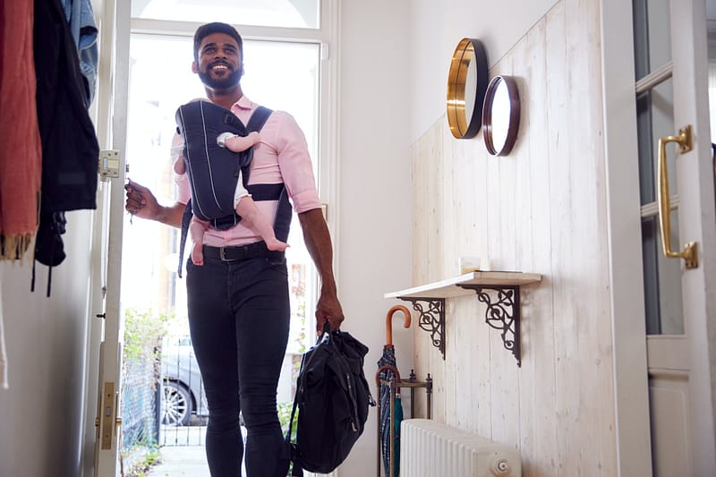 Man Carrying Baby Daughter In Sling Opens Front Door Of House